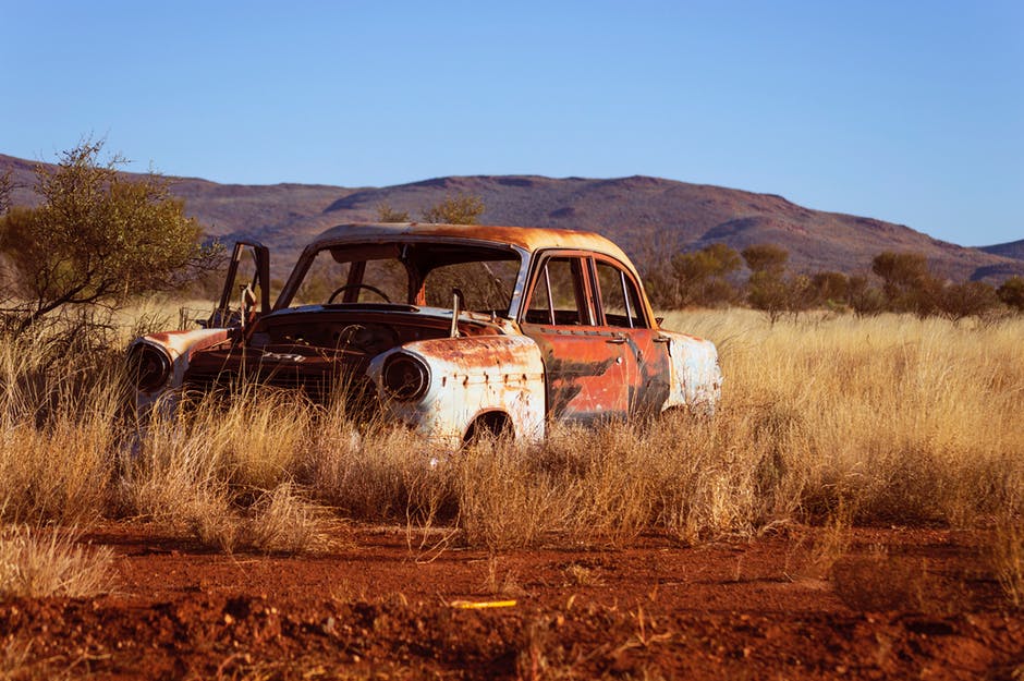 在Brown Grass上腐蚀的老式白色和红色轿车的照片