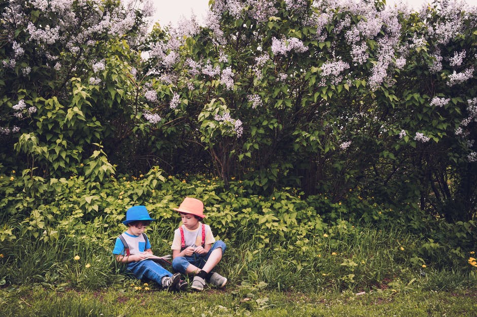 穿着白色和蓝色衬衫和蓝色牛仔裤的男孩坐在绿色的草地上