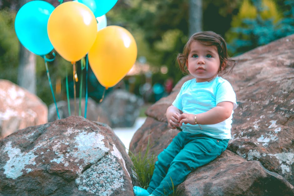 Toddler Wearing White衬衫坐在岩石旁边的黄色和蓝色气球