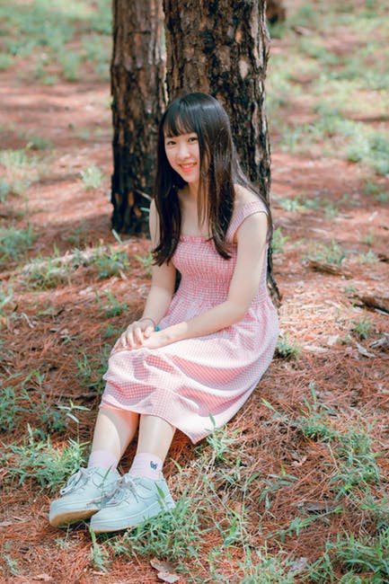 女孩和39岁；粉红色的无袖连衣裙白天坐在黑树干旁边