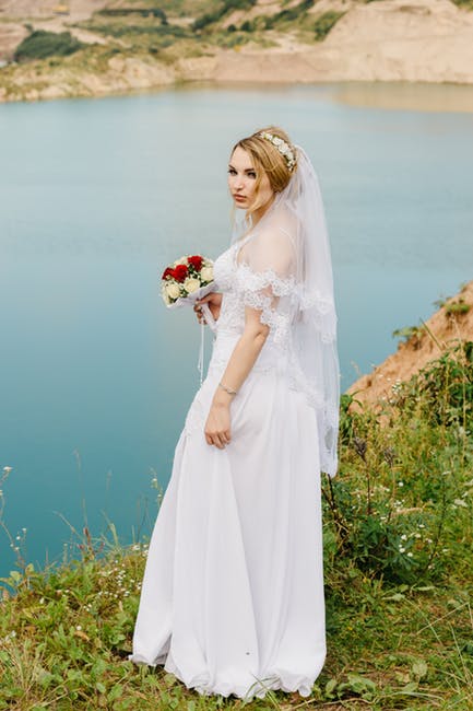 穿着婚纱的女人在湖边捧着花束