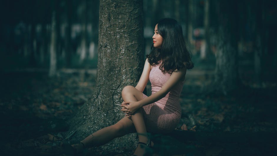 女人穿着粉红色连衣裙坐在树根上的选择性焦点摄影