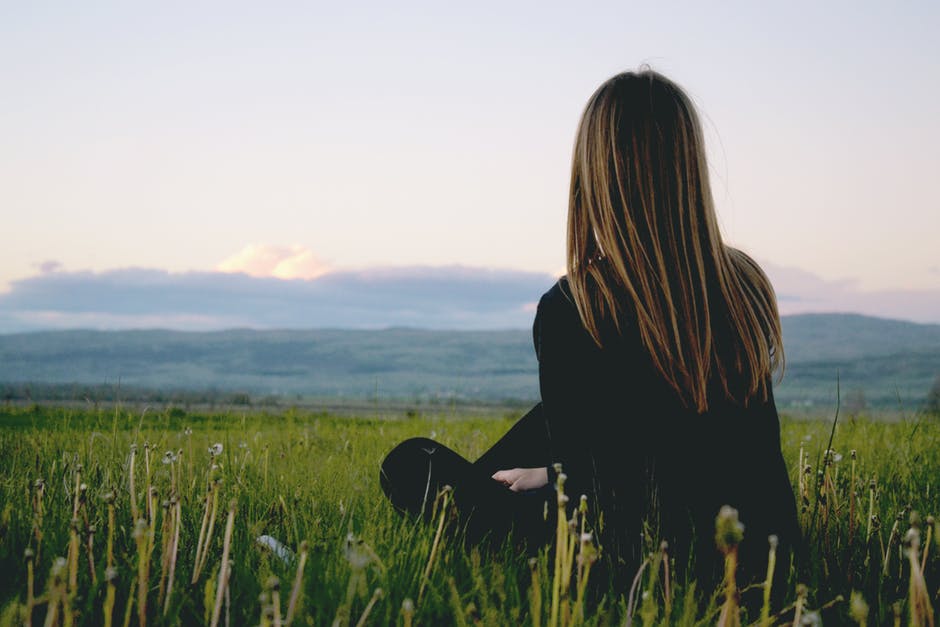 身披黑色长袖衬衫的女子坐在云天附近的青草草地上