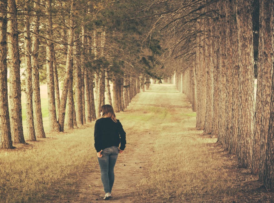 穿着黑色长袖牛仔裤和灰色牛仔裤行走在棕色森林上的女人