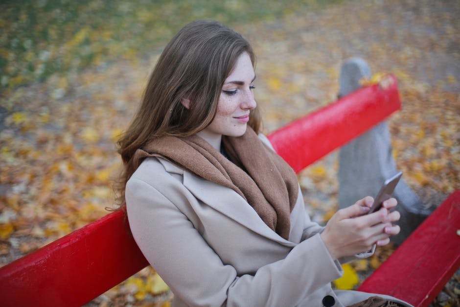 米色外套里拿着智能手机坐在长椅上的女人