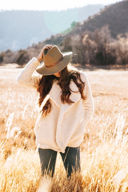 微笑的女人穿着白色的冬季夹克-棕色的牛仔帽环绕着棕色的草地