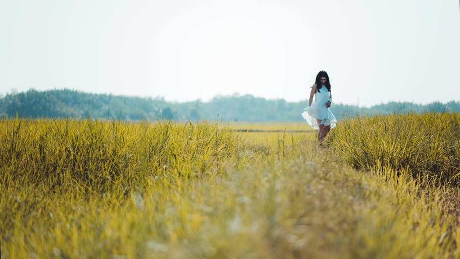 身穿白色无袖连衣裙的妇女站在绿色草地上的景深摄影