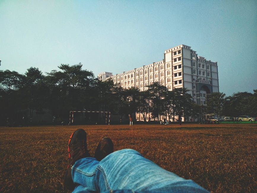 穿着蓝色斜纹棉布的人躺在棕色的草地上望着白色的多层建筑