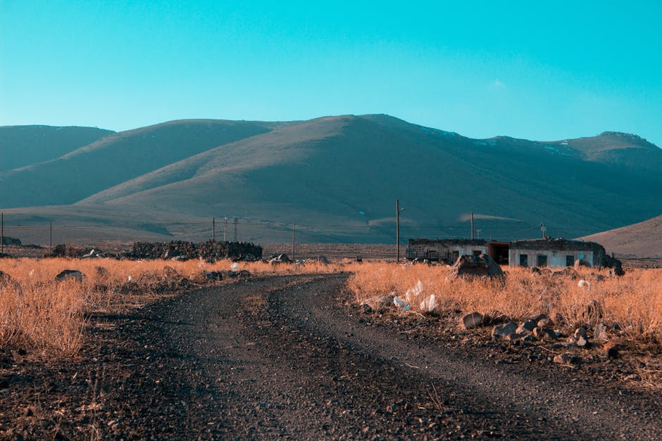 灰色的道路在棕色的草田和山的背景之间