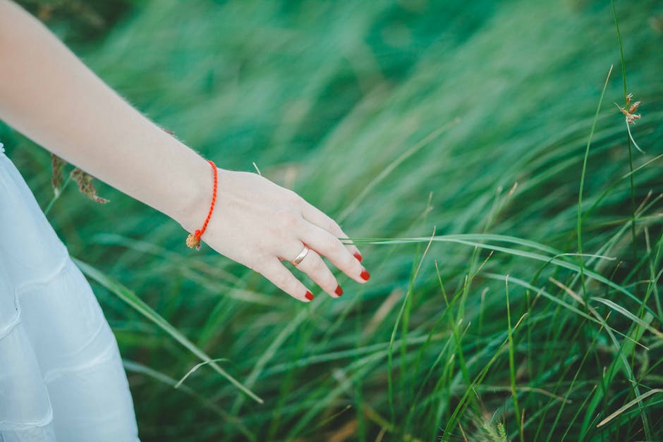 女人穿着白色裙子-橙色手镯-青草旁的红修指甲