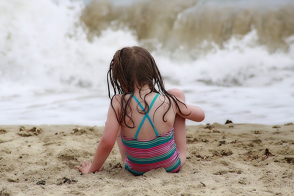 穿着色彩鲜艳的缰绳泳衣的女孩穿着棕色的沙滩