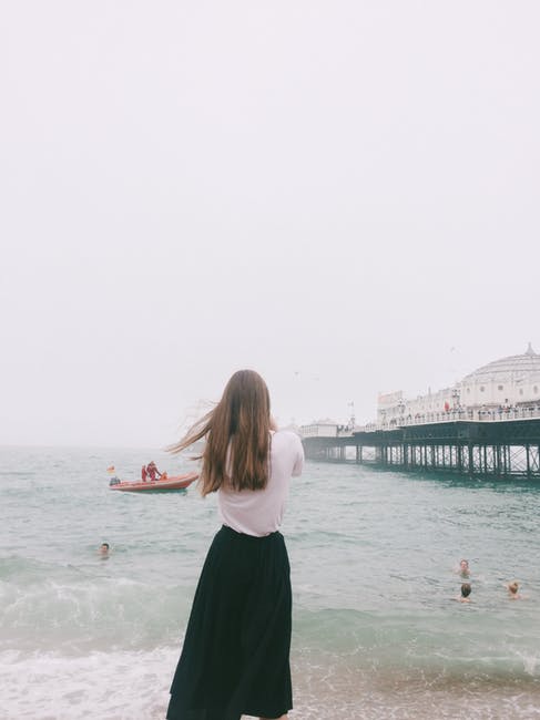 穿着白色衬衫和黑色裙子站在海边的女人