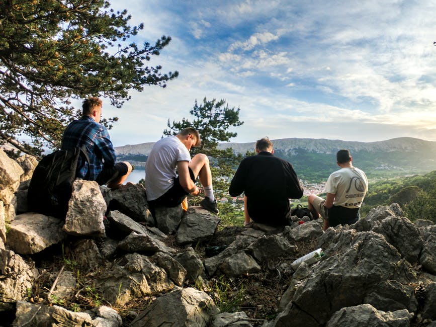 四个人坐在面向山的岩石上