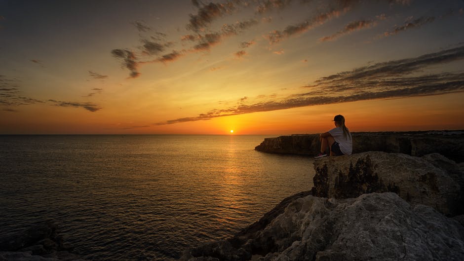 日落时坐在岩石上的人的照片