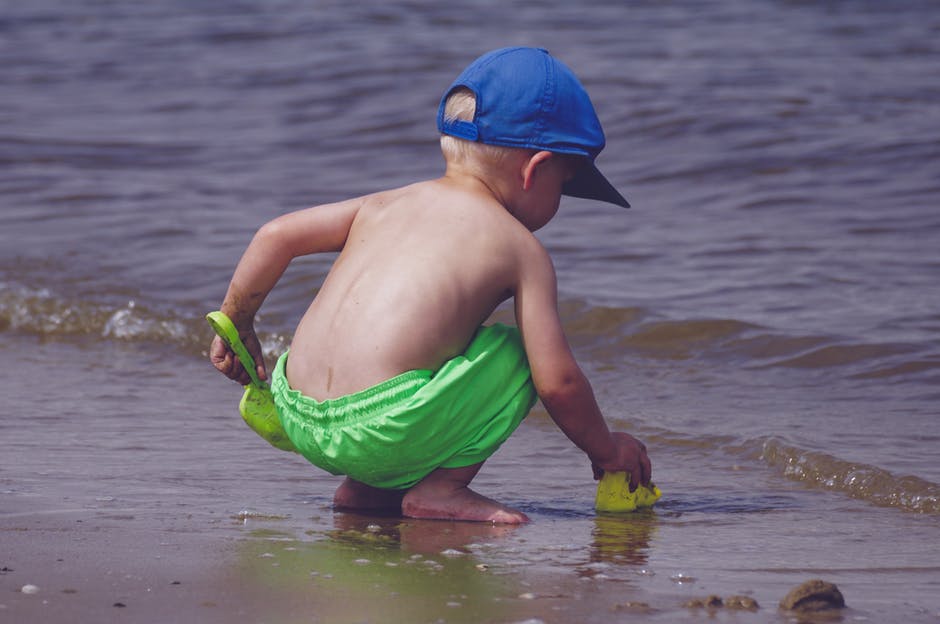 穿着蓝色帽子的男孩和绿色短裤在海滨玩耍