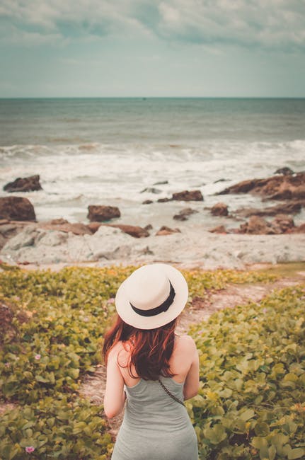 女人戴着白色帽子-站在绿色植物看海的选择性聚焦摄影