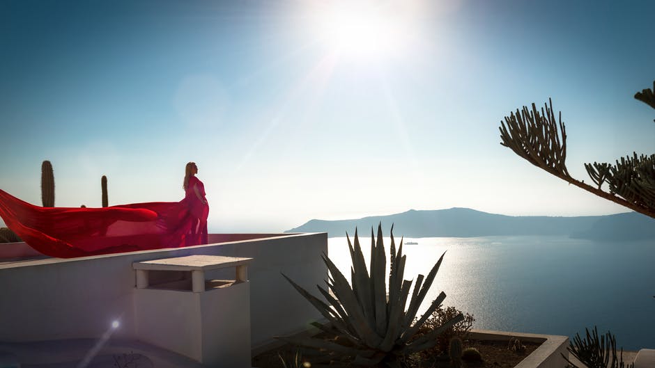身穿红色长裙的女子站在面向大海的建筑屋顶上