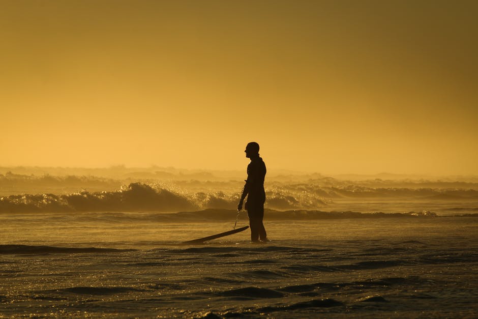 日落时站在海边的人一边拿着冲浪板