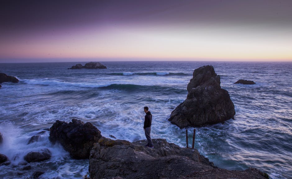 穿着黑色衬衫的人站在海水之间的岩石上
