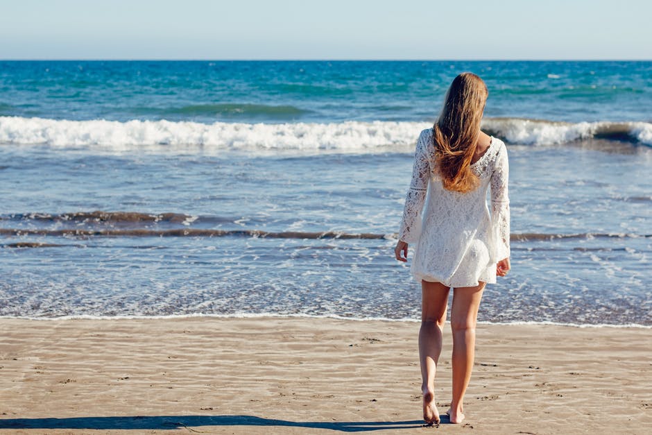 身着白色花边长袖迷你裙的棕色头发女人站在海边