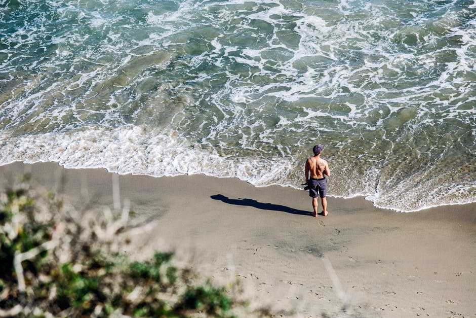 穿着灰色短裤的男人白天站在白沙海滩上