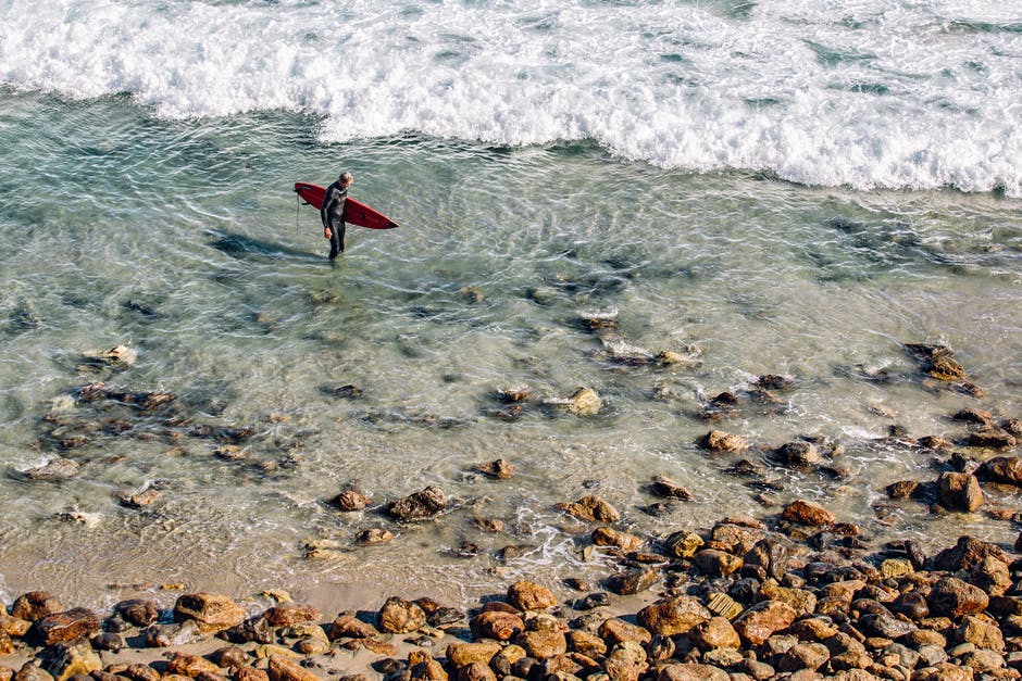白天在褐色石头附近清澈的水中拿着冲浪板的人