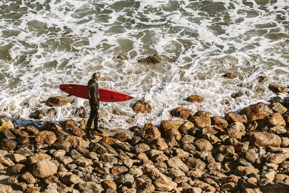Man Wearing Wetsuit与海岸上的红色冲浪板