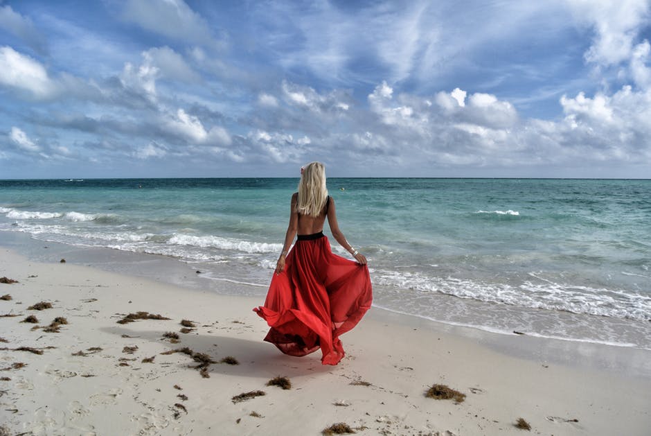 身穿红衣服的女人在蓝天白雪下漫步在海滨
