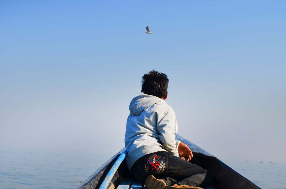 男人穿着灰色的帽衫和黑色的裤子坐在船中间看着天空中的鸟