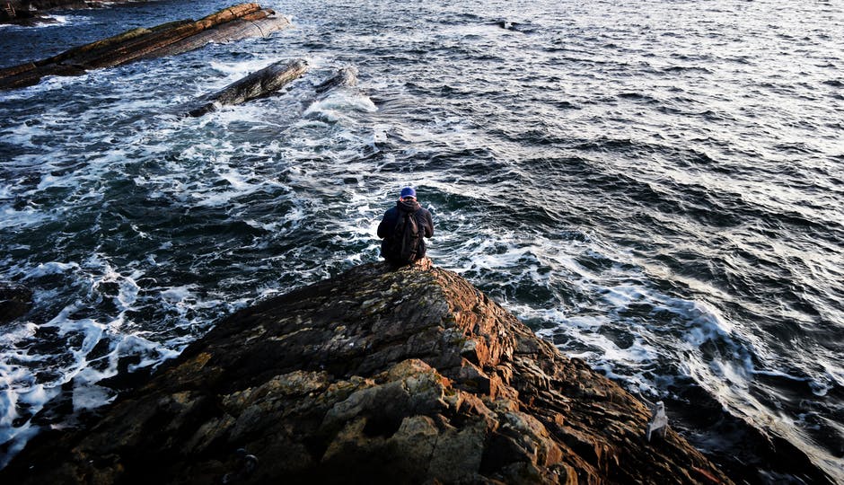 坐在近海岩石上的人的摄影